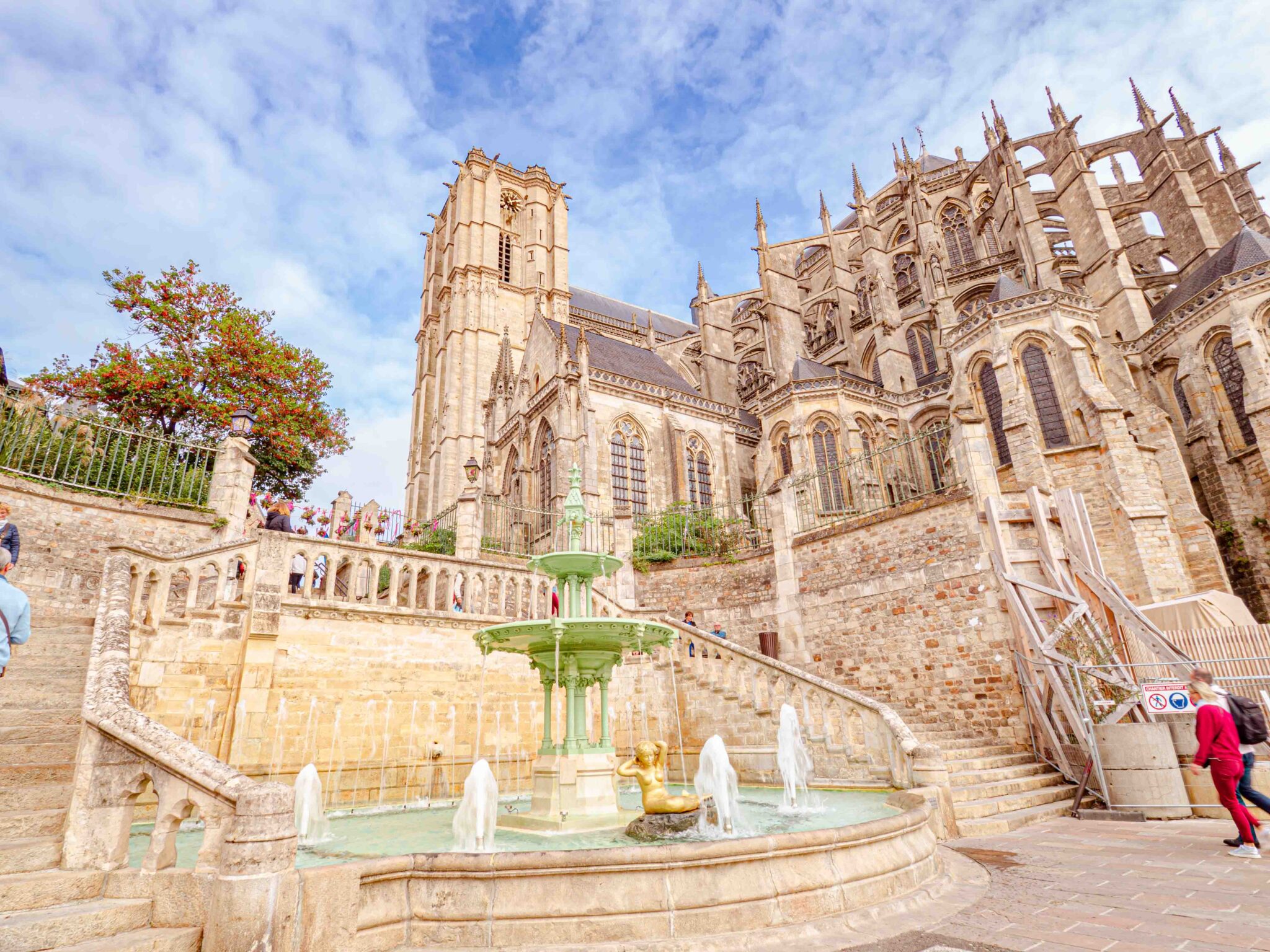 Cette image présente une vue spectaculaire de la Cathédrale Saint-Julien du Mans, un exemple frappant de l'architecture gothique et romane. L'édifice religieux se dresse majestueusement dans l'arrière-plan, avec son unique tour s'élevant vers le ciel. Au premier plan, la fontaine du Jet d'eau offre un point d'intérêt dynamique. Les gouttelettes d'eau scintillent à la lumière du jour, ajoutant un élément de mouvement et de fraîcheur à la scène. Ensemble, la cathédrale et la fontaine créent une image à la fois historique et vivante de Le Mans.