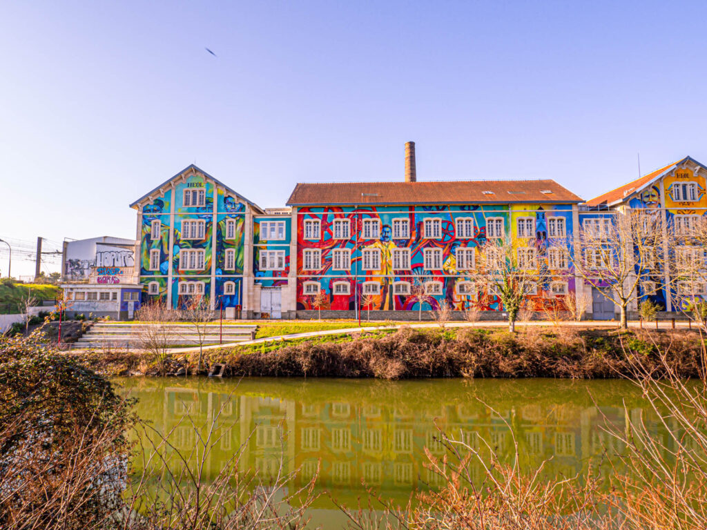 Cette image capture une fresque impressionnante intitulée "Heol", créée sur les murs de l'ancienne manufacture des tabacs du Mans. L'œuvre d'art est située près de la Sarthe dont les eaux miroitantes reflètent la magnificence colorée de la fresque. L'artiste a transformé le mur de l'ancienne manufacture en une toile vibrante, ajoutant une nouvelle dimension culturelle à cette partie historique de la ville. La fresque semble donner vie à l'environnement urbain environnant, offrant un point d'intérêt visuel saisissant pour les passants. Cette photo a été capturée avec brio par ParisianGeek, qui a su mettre en valeur les détails et les couleurs éclatantes de cette fresque de street art.