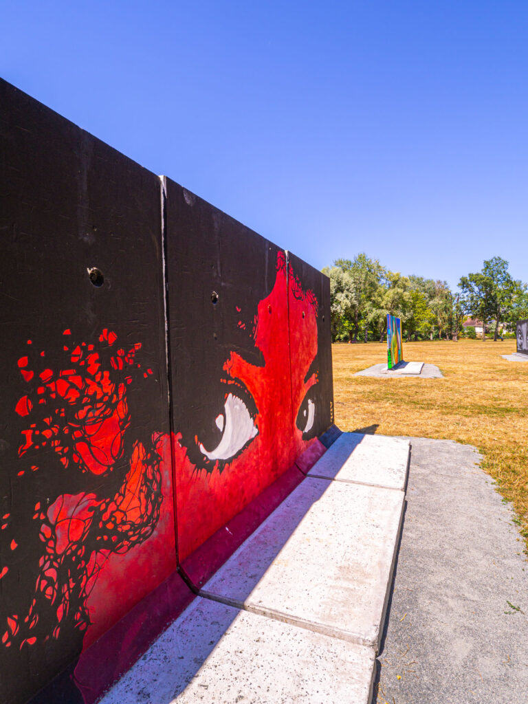 Photographie capturant une série de murs installés dans le parc du Gué de Maulny au Mans, exhibant un éventail de street art vibrant et diversifié créé pendant le festival Plein Champ. Ces murs, transformés en toiles urbaines dynamiques, sont ornés de différentes œuvres d'art de rue, chacune exhibant un style unique, une explosion de couleurs et un ensemble complexe de motifs. L'art représente une fusion d'histoires visuelles, mettant en valeur la créativité des artistes locaux et leur engagement envers l'expression culturelle. Situé en plein cœur du parc, cet assemblage artistique crée un contraste frappant avec le paysage naturel environnant, démontrant le mélange fascinant de l'art et de la nature au sein de la ville du Mans.